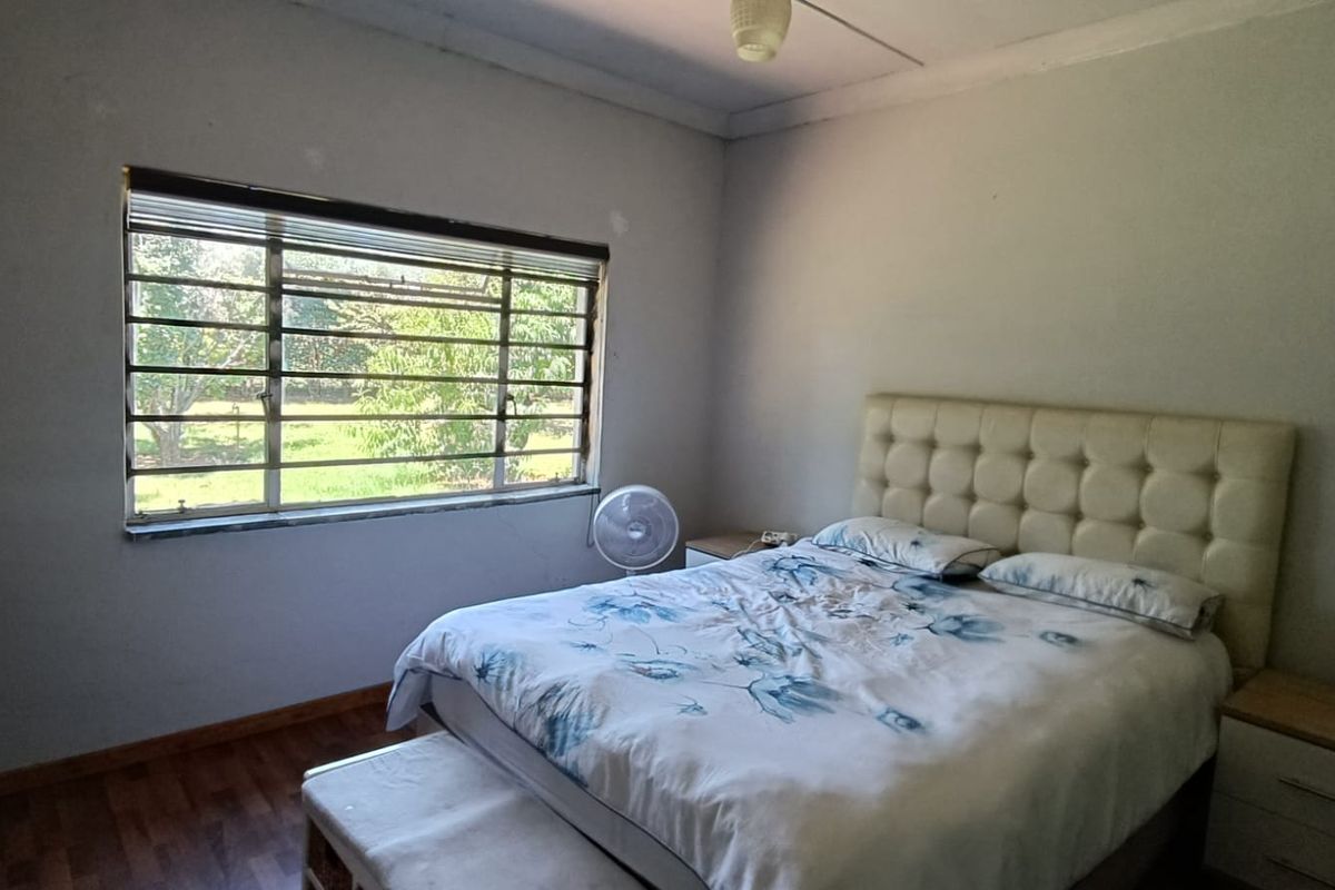 A bedroom featuring parquet flooring, a large window with metal burglar bars, and a neutral color palette.