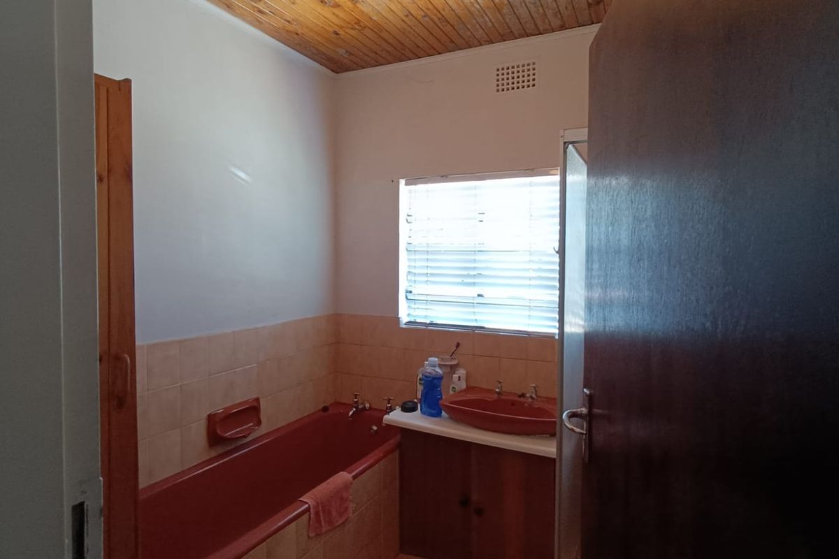 A dated bathroom featuring a colored bathtub and vanity basin, with a wooden ceiling and tiled splashbacks.
