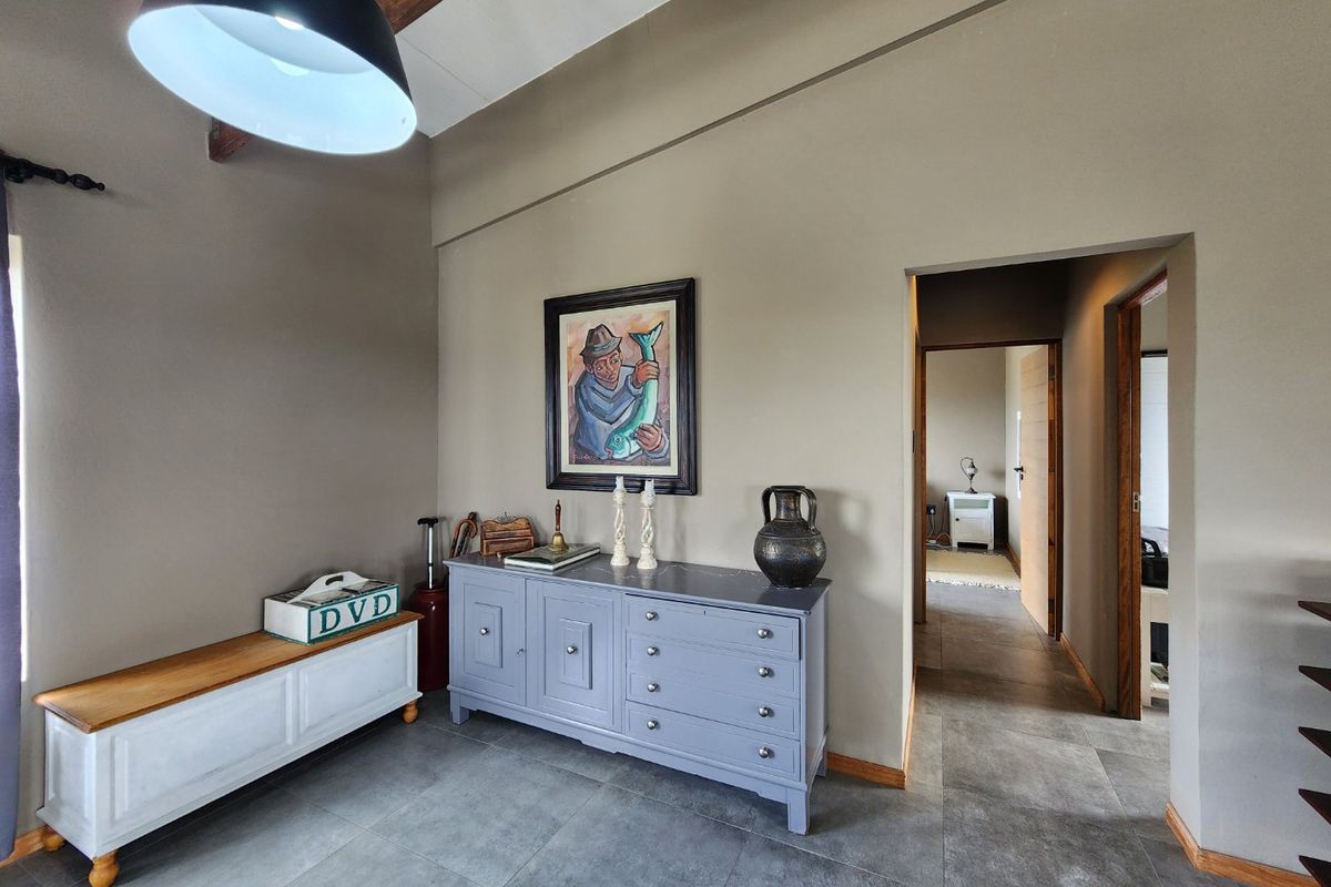 A spacious living area featuring high vaulted ceilings with exposed timber beams, tiled flooring, and neutral wall tones, leading into a connecting hallway.