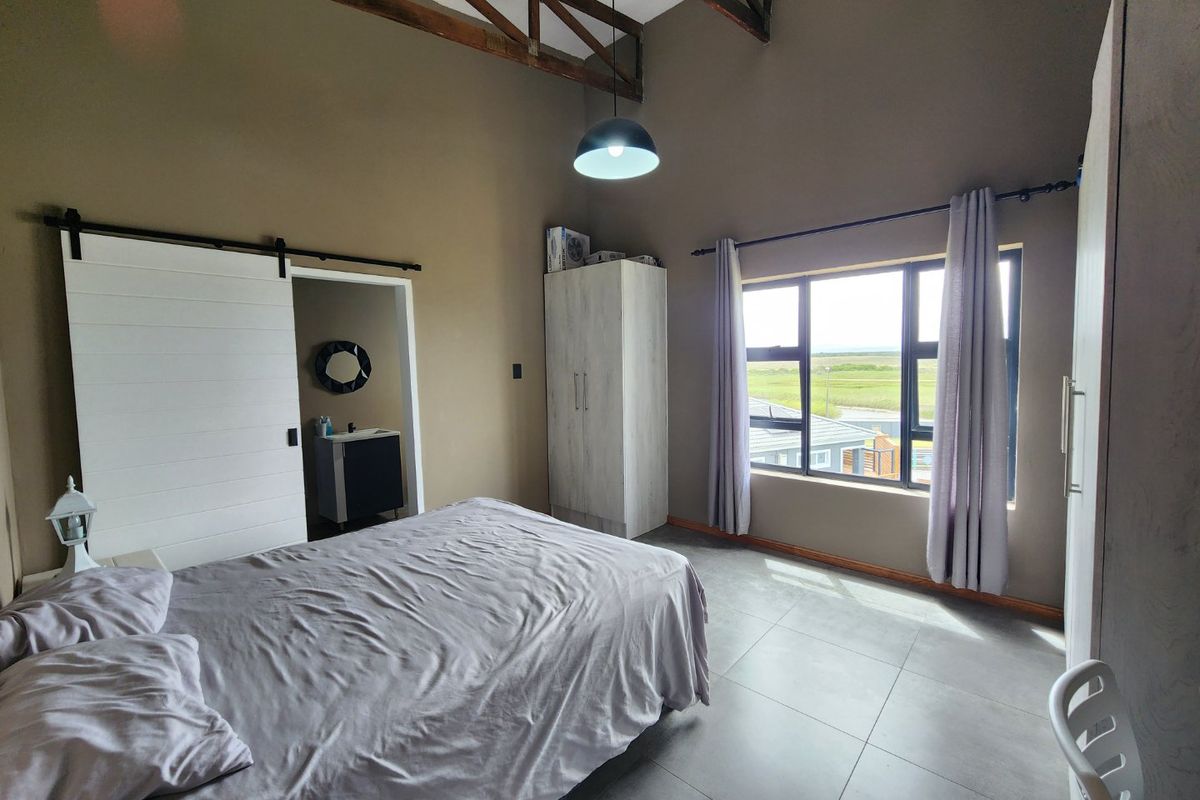 Spacious bedroom featuring high vaulted ceilings with exposed timber trusses, large windows with scenic views, tiled flooring, and an en-suite bathroom with sliding door.