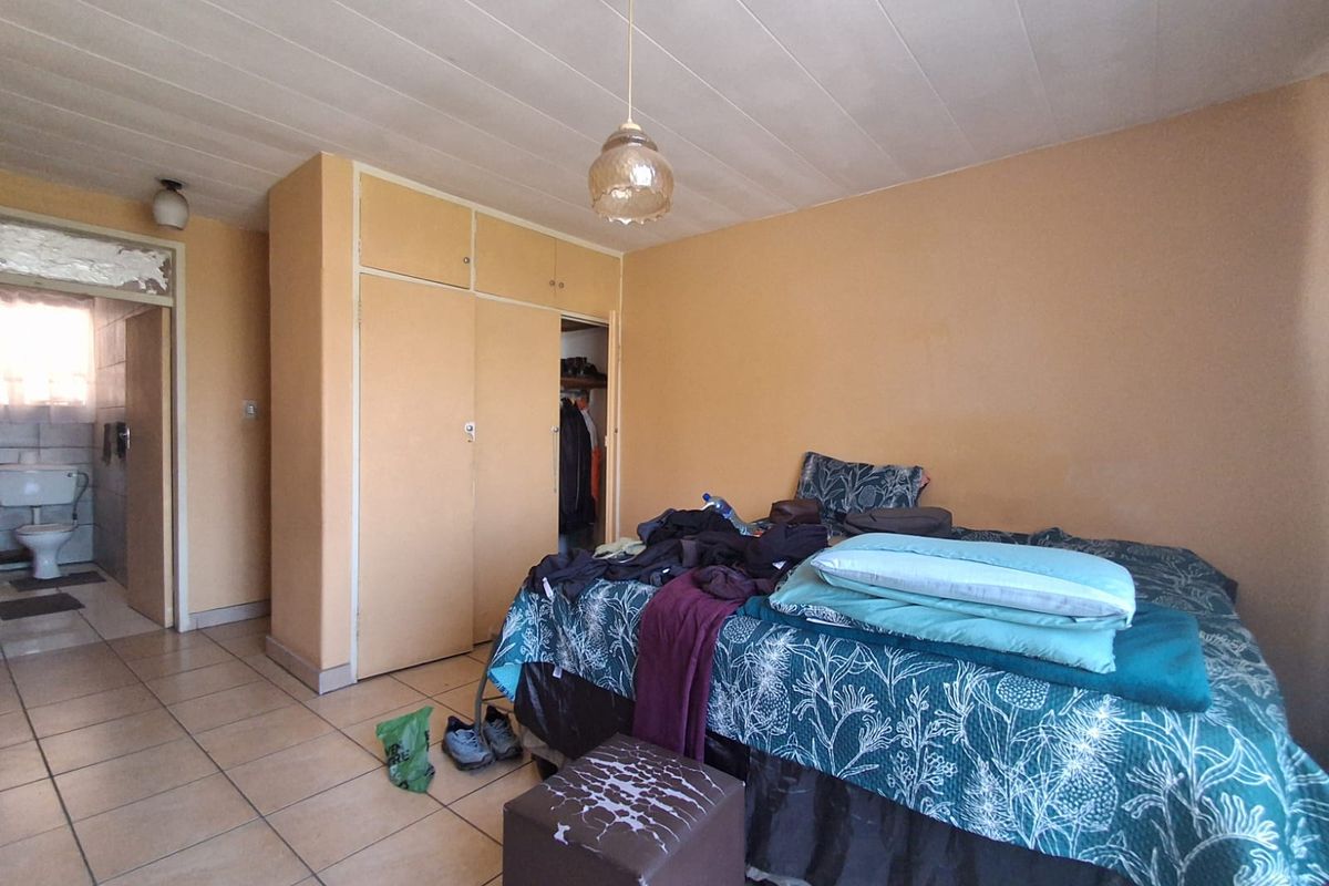 A bedroom featuring built-in cupboards and tiled flooring, with an adjacent bathroom visible through the doorway.