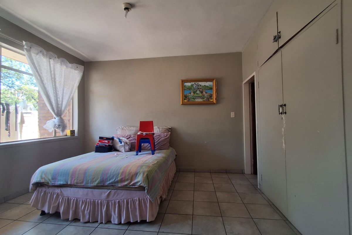 A bedroom featuring tiled flooring, built-in cupboards, and a large window providing natural light.