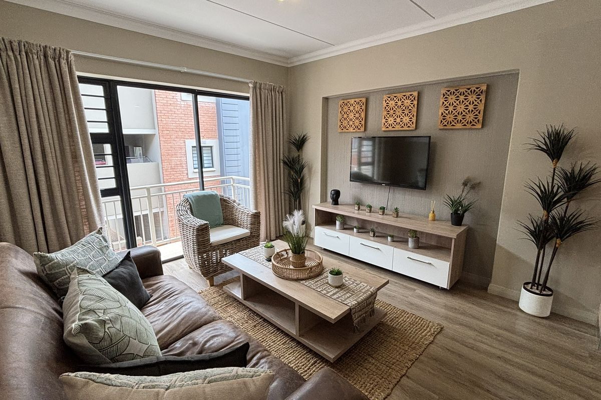 A well-maintained living room featuring a recessed media wall, laminate flooring, and large sliding glass doors leading to a private balcony.