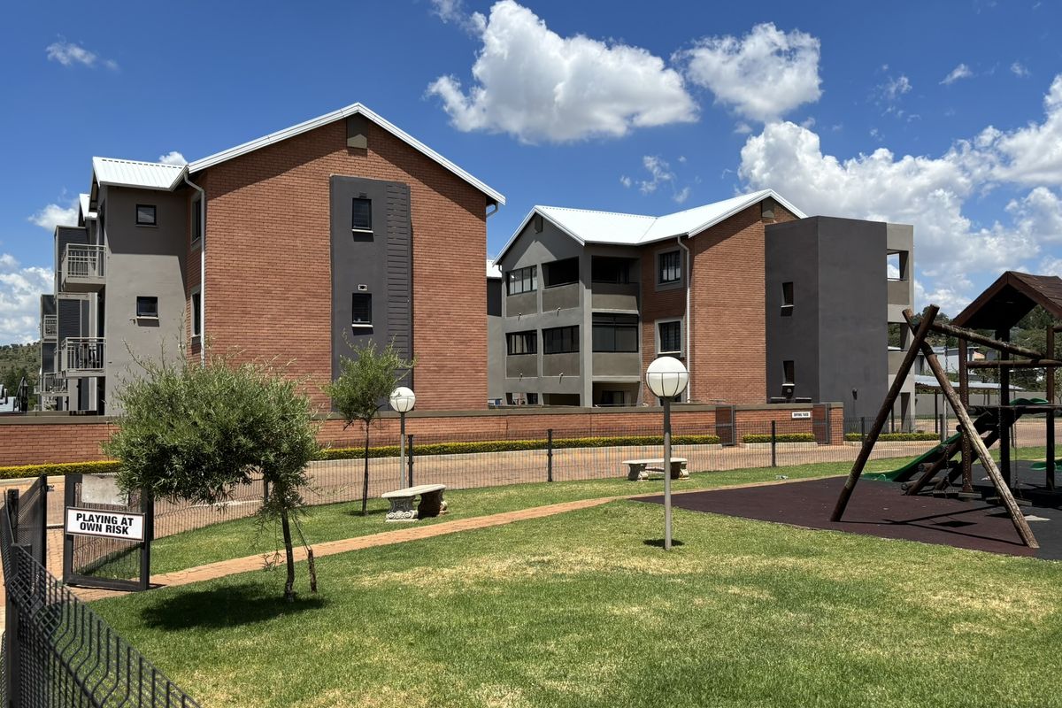 Exterior view of a modern brick apartment complex featuring a communal garden area with a children's playground and paved walkways.