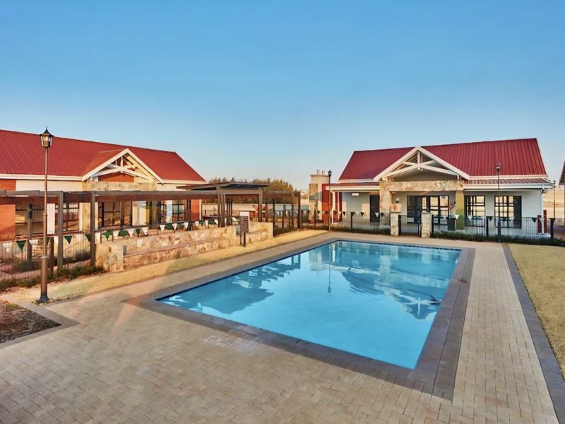 A well-maintained communal swimming pool area featuring paved decking, stone-clad accents, and modern pergola structures set against residential buildings.
