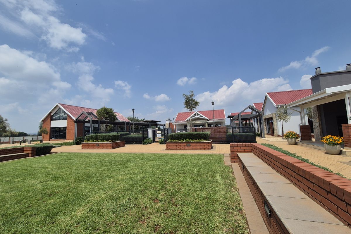A well-maintained communal outdoor area featuring brick retaining walls, paved pathways, manicured lawns, and modern buildings with metal roofing.