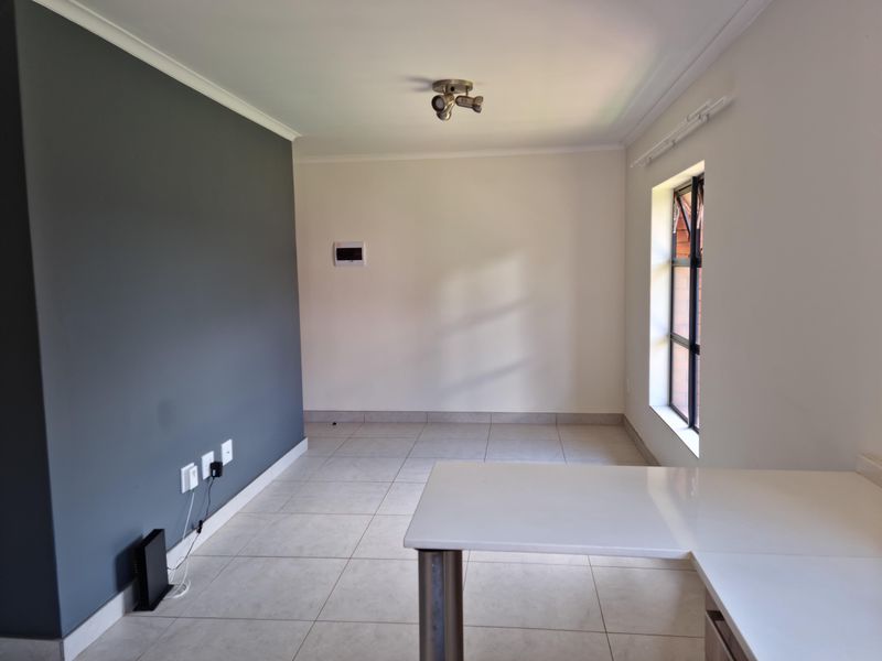 An empty living area featuring tiled floors, a dark grey accent wall, and a built-in desk, offering a clean and versatile space.