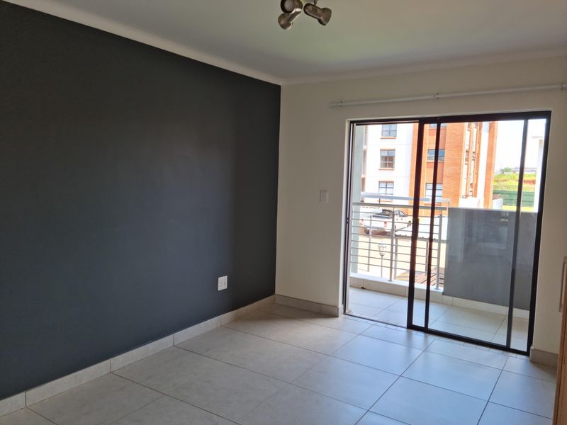 An empty living room featuring large format floor tiles, a dark grey accent wall, and a sliding glass door leading to a balcony.