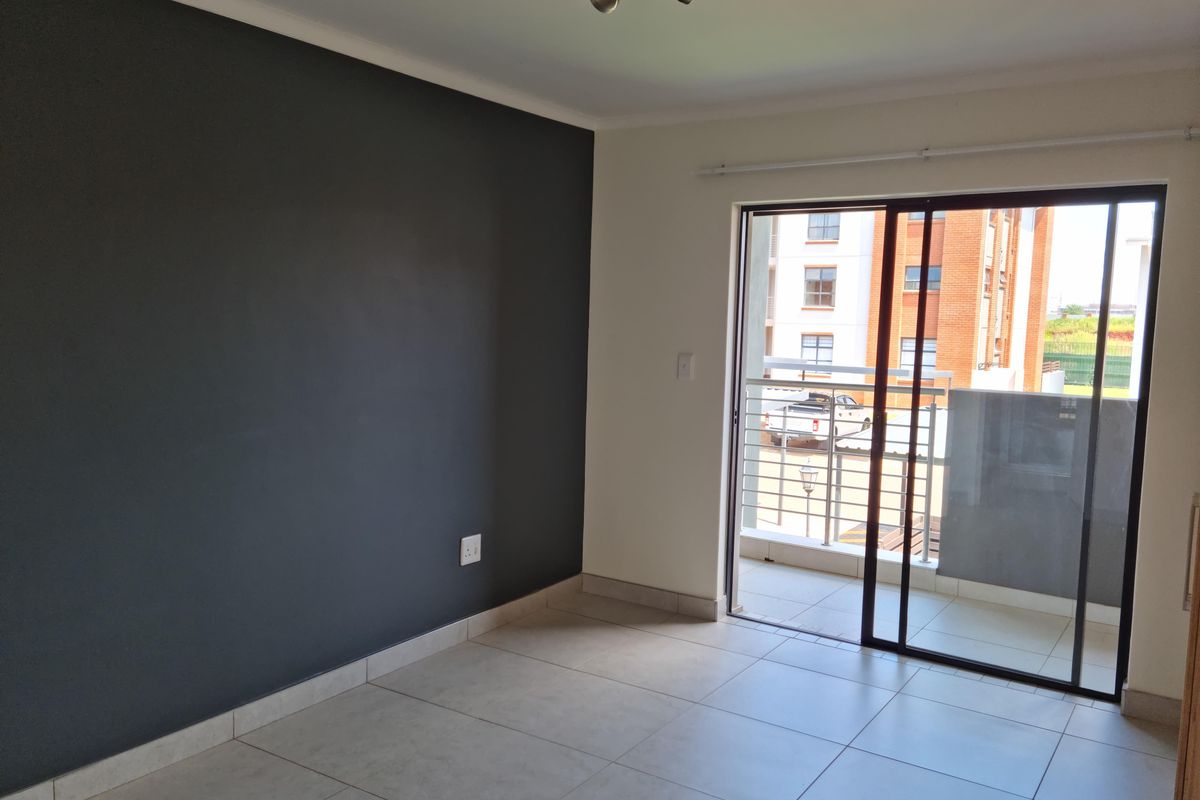 An empty living room featuring large format floor tiles, a dark grey accent wall, and a sliding glass door leading to a balcony.