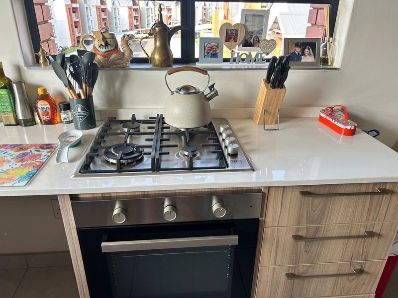 A well-maintained kitchen area featuring a modern gas hob, built-in oven, stone countertops, and contemporary wood-finish cabinetry.