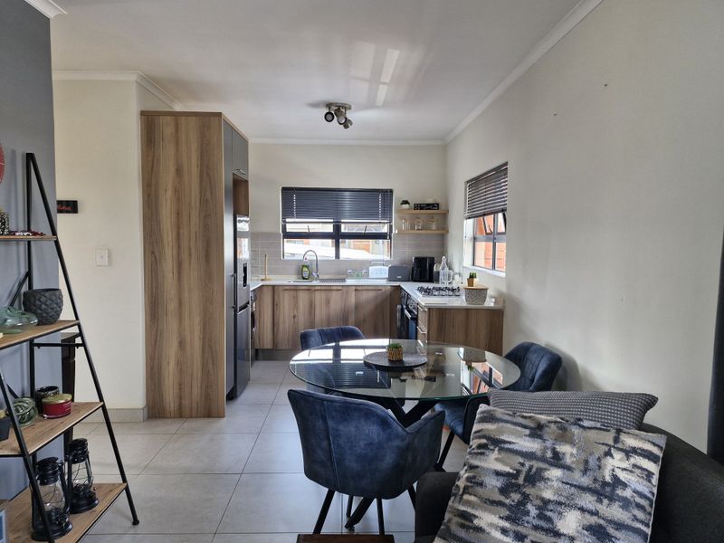 Modern open-plan kitchen and dining area featuring wood-finish cabinetry, gas hob, oven, and neutral tiled flooring, creating a functional and cohesive living space.