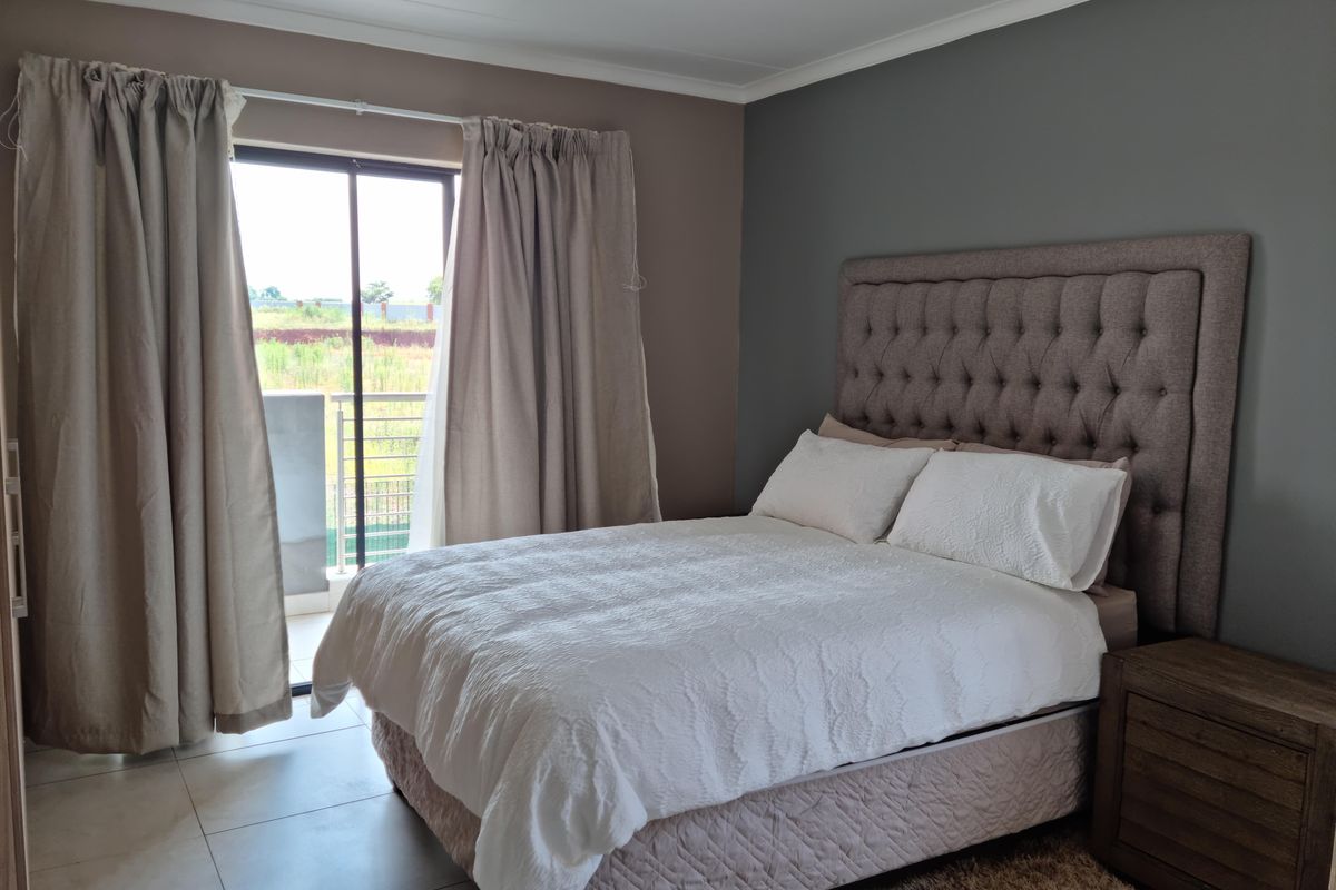 A well-maintained bedroom featuring neutral wall tones, tiled flooring, and direct access to a private balcony through a sliding glass door.