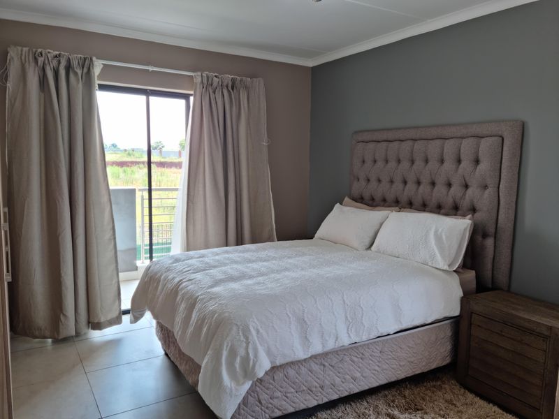 A well-maintained bedroom featuring neutral wall tones, tiled flooring, and direct access to a private balcony through a sliding glass door.