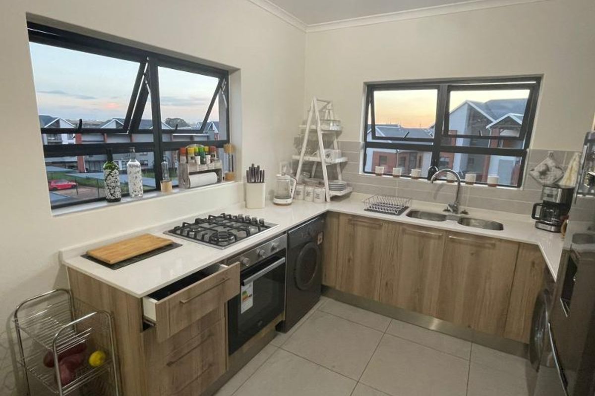 Modern kitchen featuring light wood cabinetry, stone countertops, gas hob, built-in oven, and double sink with tiled flooring and splashback.
