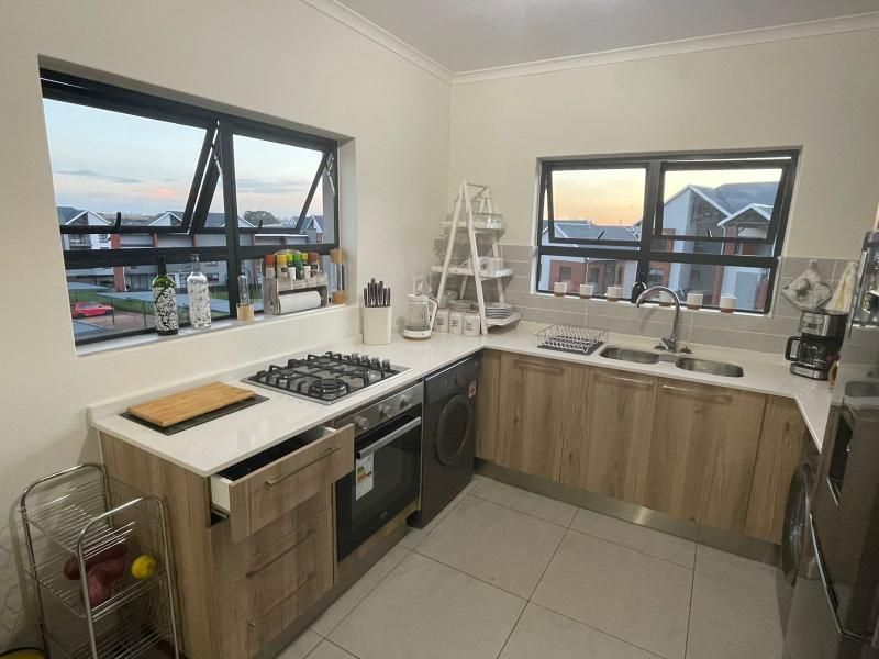 Modern kitchen featuring light wood cabinetry, stone countertops, gas hob, built-in oven, and double sink with tiled flooring and splashback.