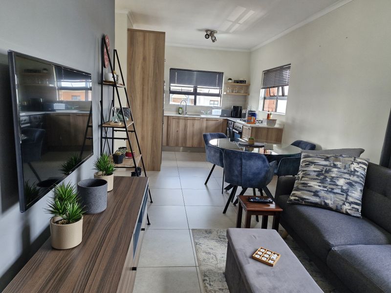 An open-plan living and kitchen area featuring modern wood-finish cabinetry, tiled flooring, and neutral wall tones, creating a functional and cohesive living space.