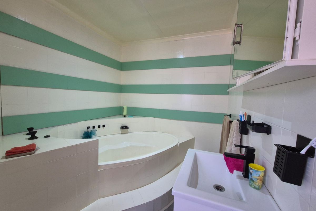 A functional bathroom featuring a built-in corner bathtub with tiled surround and a modern vanity basin with black fixtures.
