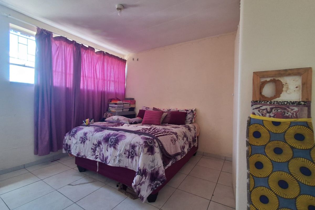 A bedroom featuring tiled flooring and a large window with curtain fixtures, providing natural light to the space.