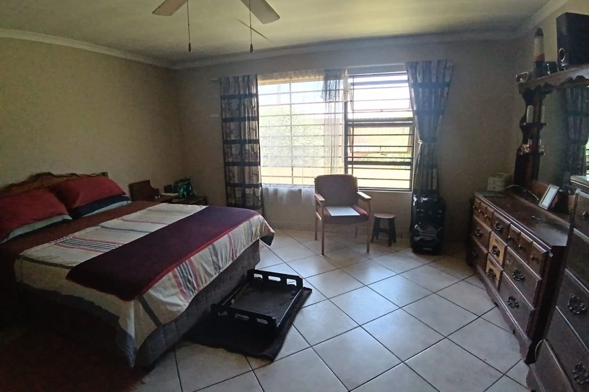 A spacious bedroom featuring tiled flooring, a ceiling fan, and large windows with security bars, providing ample natural light.