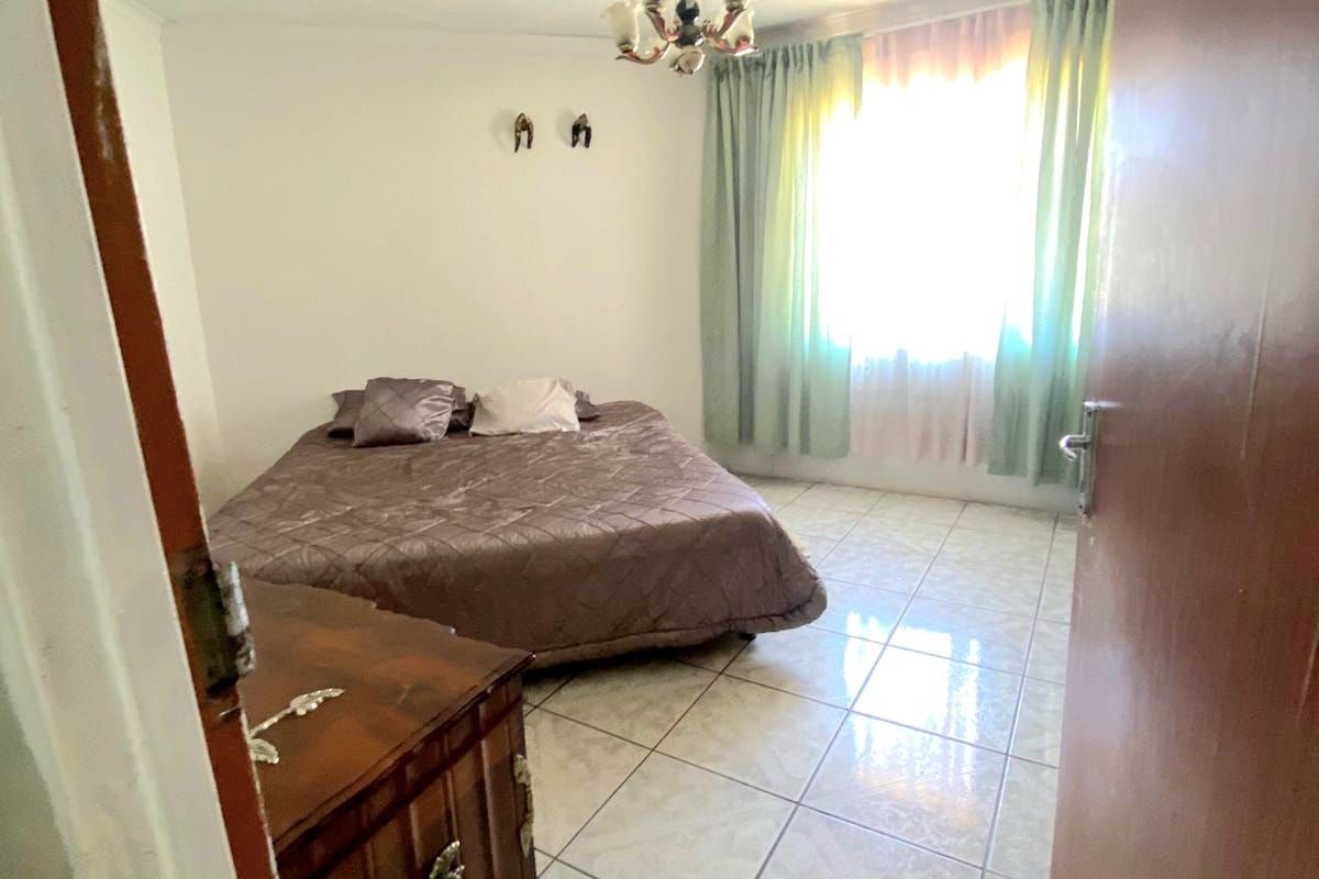 A bedroom featuring tiled flooring, a central light fixture, and a window with curtains, providing a functional and well-lit sleeping space.