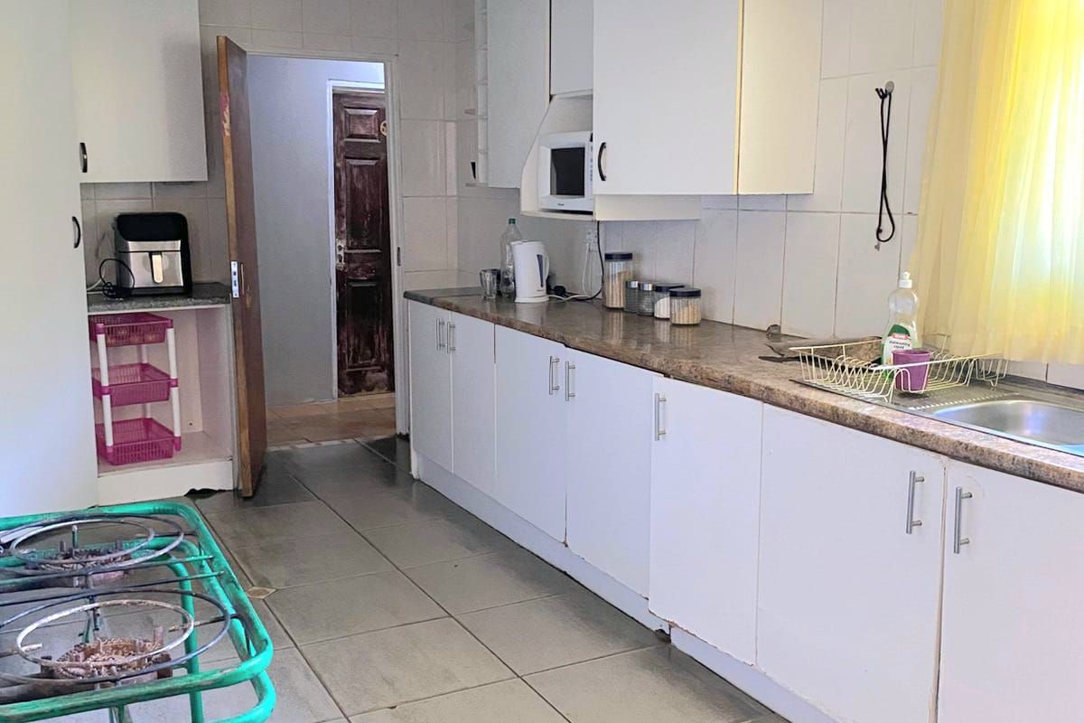 A functional kitchen featuring white cabinetry, laminate countertops, a stainless steel sink, and tiled flooring, offering a practical layout for daily meal preparation.