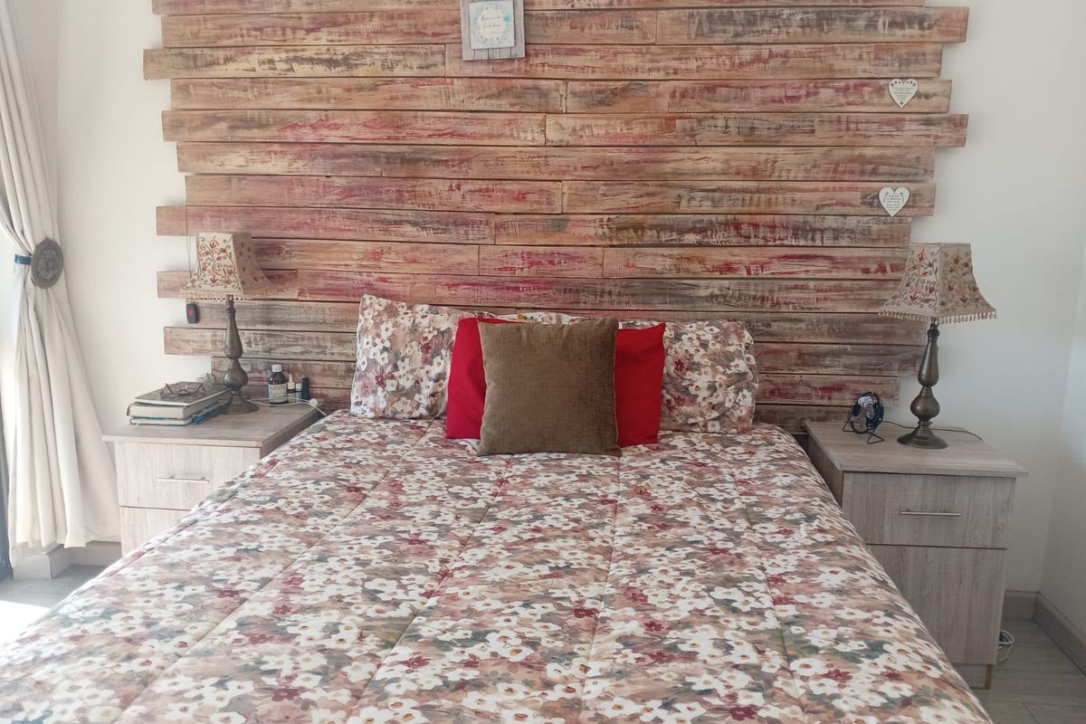A bedroom featuring a rustic timber-plank feature wall behind the bed area, complemented by neutral tiled flooring.