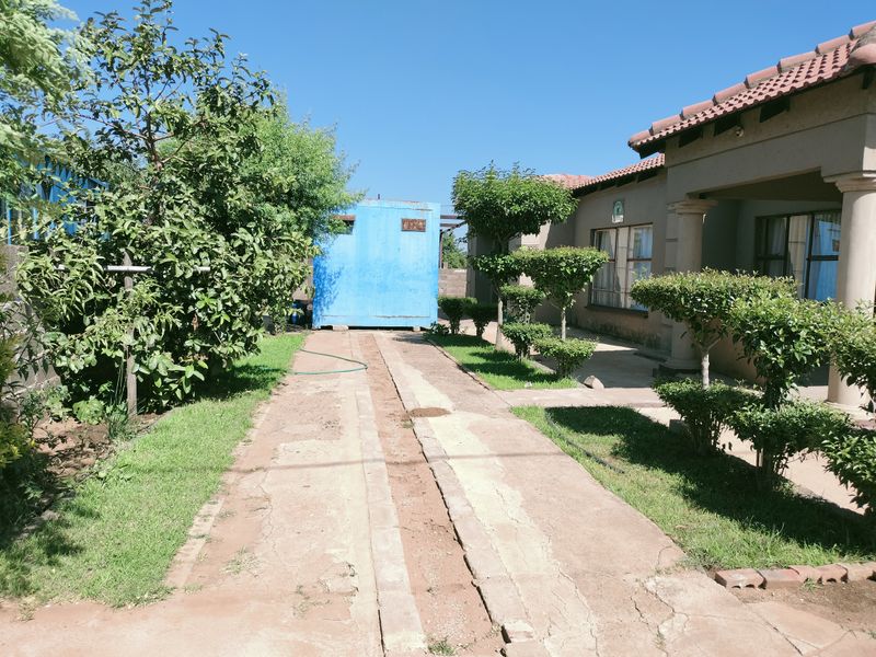 A view of the side exterior area featuring a concrete driveway, landscaped shrubs, and a detached blue storage structure.