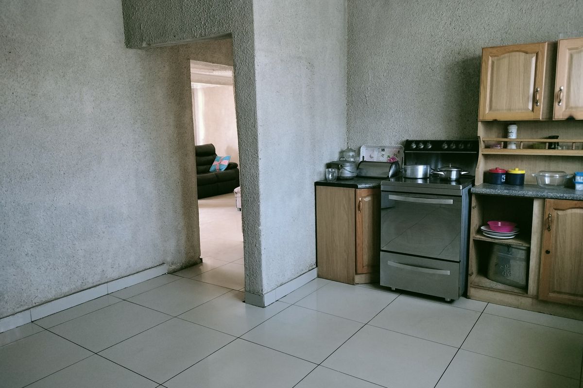 A functional kitchen area featuring tiled flooring, built-in wooden cabinetry, and a freestanding stove, with an open doorway leading to an adjacent living space.