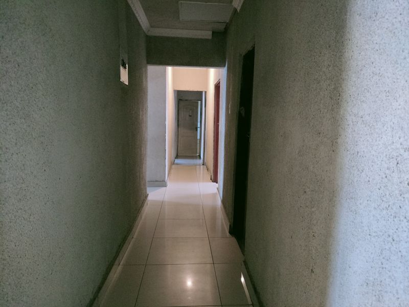 A narrow interior hallway featuring tiled flooring and textured wall finishes, providing access to multiple rooms within the property.