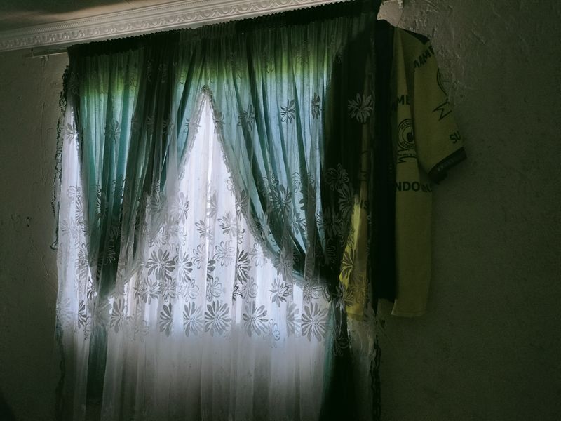 A bedroom window featuring decorative curtain rails and layered curtains, set against a textured wall with visible signs of wear.
