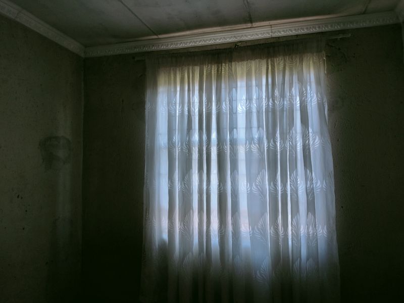 A dimly lit bedroom featuring textured walls with visible signs of wear and decorative ceiling cornicing.