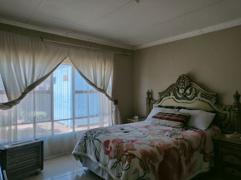 A bedroom featuring tiled flooring, decorative ceiling cornicing, and large windows allowing natural light.