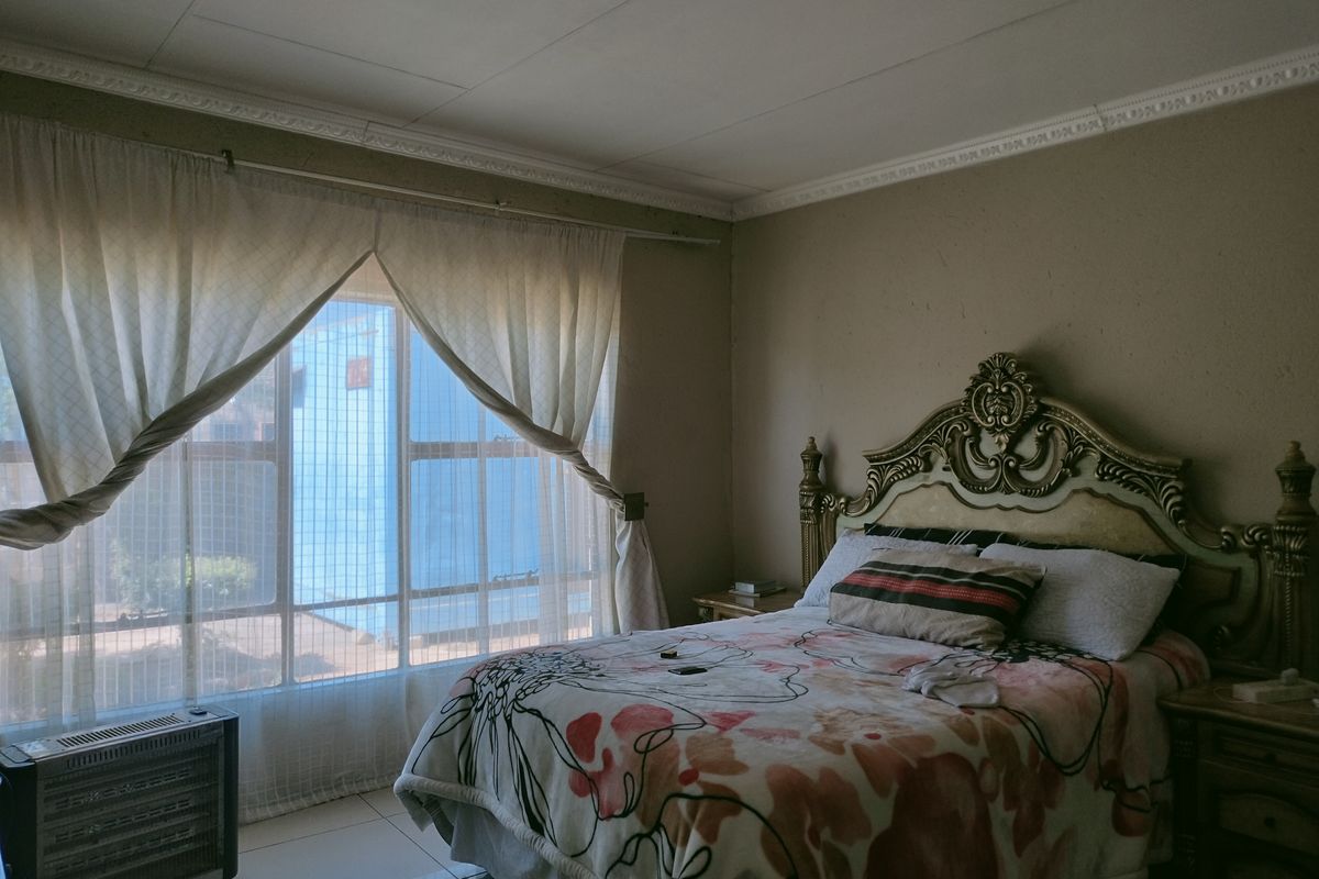 A bedroom featuring tiled flooring, decorative ceiling cornicing, and large windows allowing natural light.