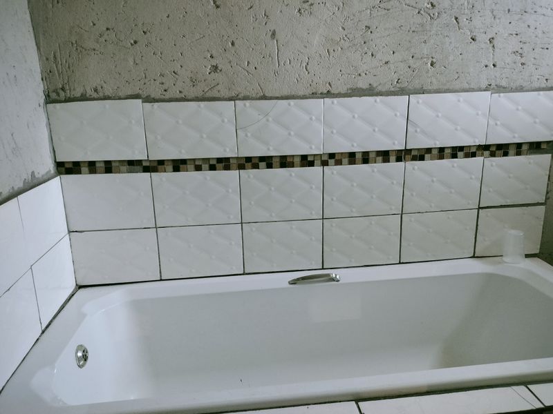 A bathroom featuring a built-in bathtub with partially tiled walls and unfinished plasterwork above, requiring completion and final finishes.