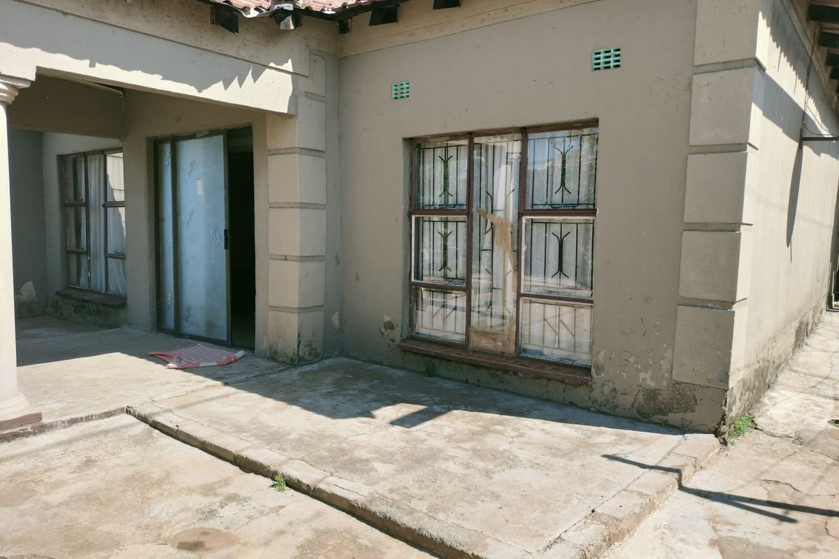 Exterior view of the house featuring a concrete patio area, sliding glass door, and windows with security bars.
