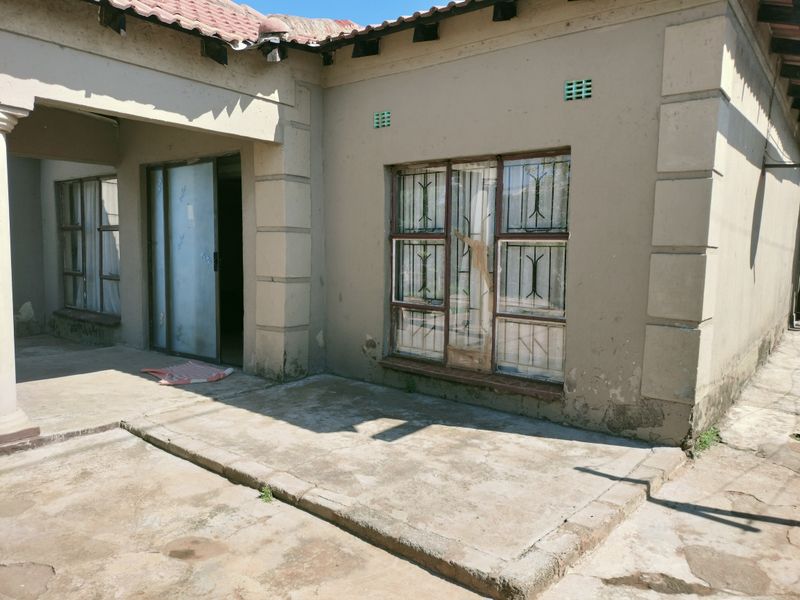 Exterior view of the house featuring a concrete patio area, sliding glass door, and windows with security bars.