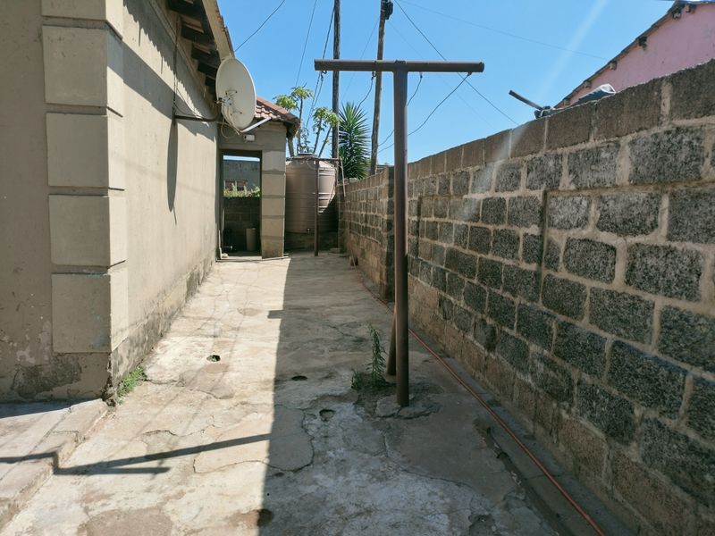 A narrow side exterior area featuring a concrete pathway, a boundary wall, a water storage tank, and a metal washing line structure.