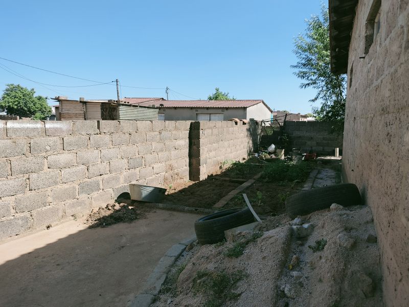 A side yard area featuring a concrete block boundary wall and unpaved ground, offering potential for landscaping or outdoor development.