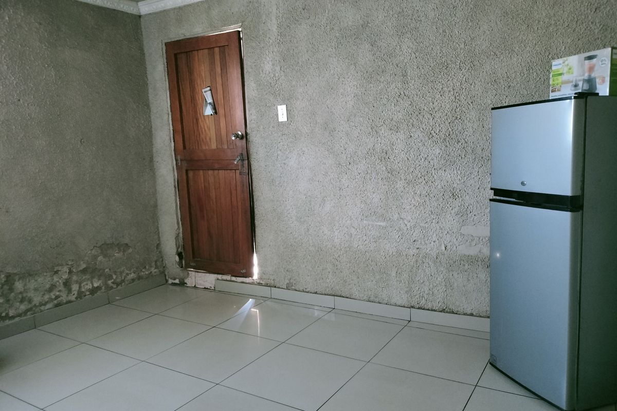 An interior room featuring tiled flooring, a wooden door, and unfinished textured wall surfaces requiring repair and cosmetic attention.