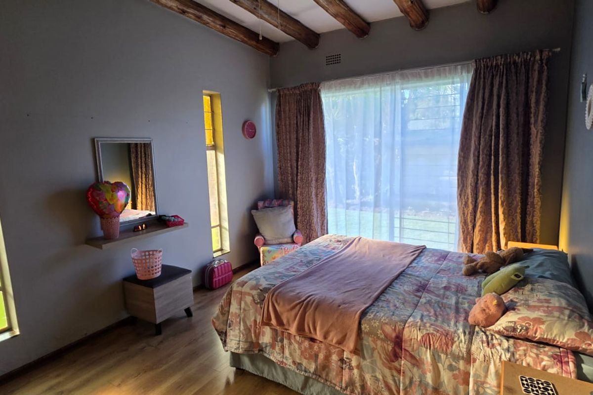 A bedroom featuring exposed timber ceiling beams, laminate flooring, and large windows providing natural light.