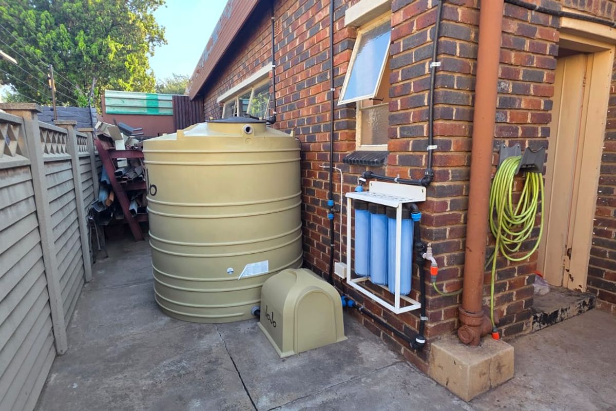 Exterior side area featuring a large water storage tank, integrated water filtration system, and brick wall construction.