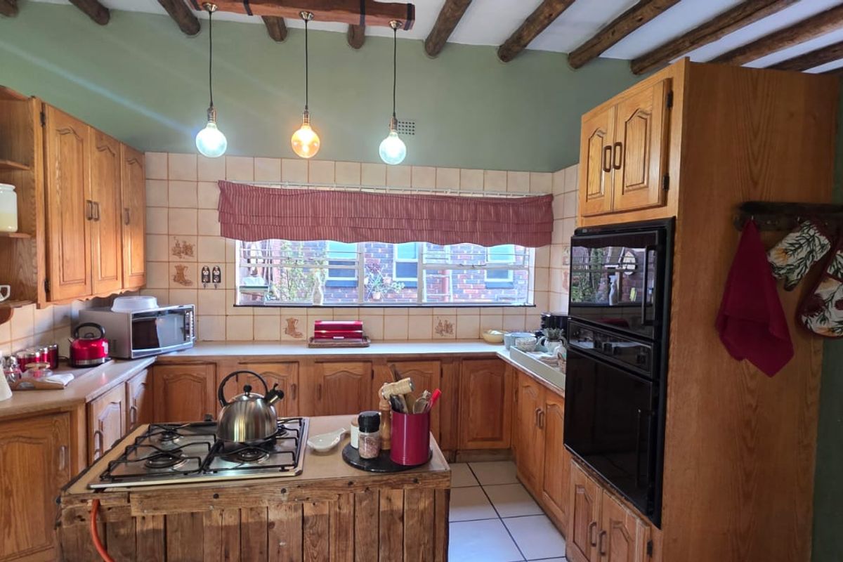 A functional kitchen featuring timber cabinetry, a central island with a gas hob, built-in oven, and exposed timber ceiling beams.