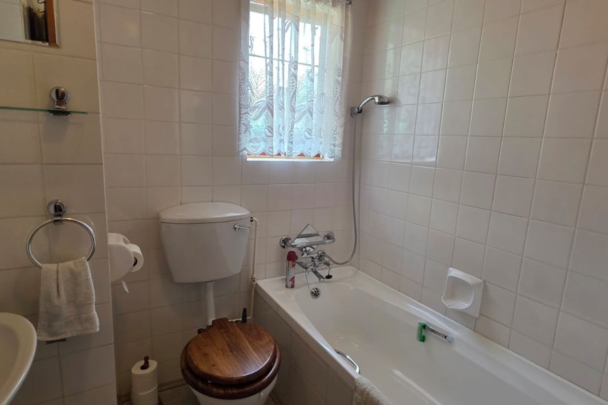 A functional bathroom featuring a standard bathtub with shower mixer, wall-mounted basin, and toilet, finished with classic white wall tiles.