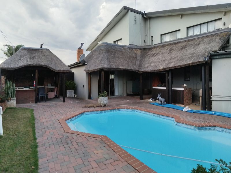 Outdoor entertainment area featuring a swimming pool, brick paving, and a covered patio with a thatched roof and built-in braai facilities.