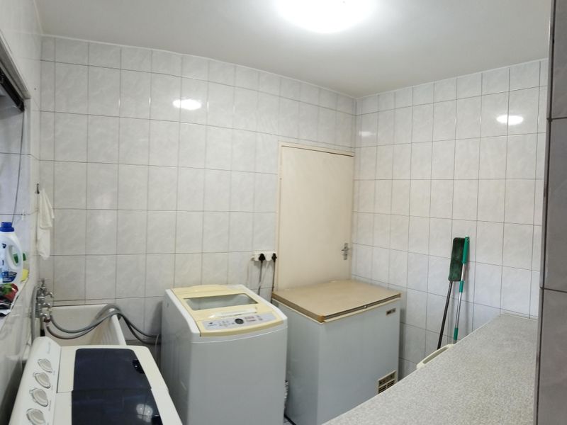 A functional laundry room featuring fully tiled walls, a built-in sink, and ample counter space for utility tasks.