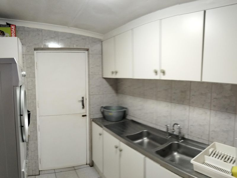 Functional laundry room featuring fitted white cabinetry, a double stainless steel sink, tiled splashbacks, and tiled flooring.