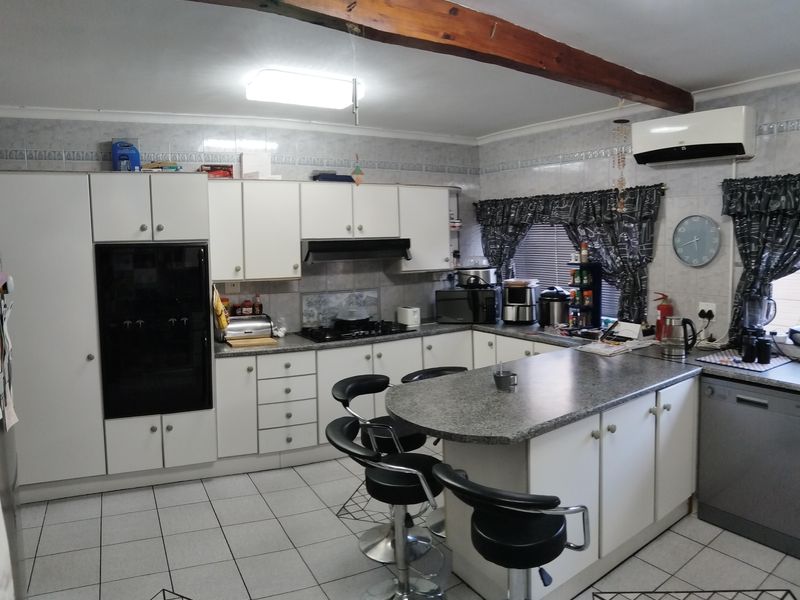 A functional kitchen featuring white cabinetry, granite countertops, a built-in oven, gas hob, and an exposed timber ceiling beam, with tiled flooring throughout.