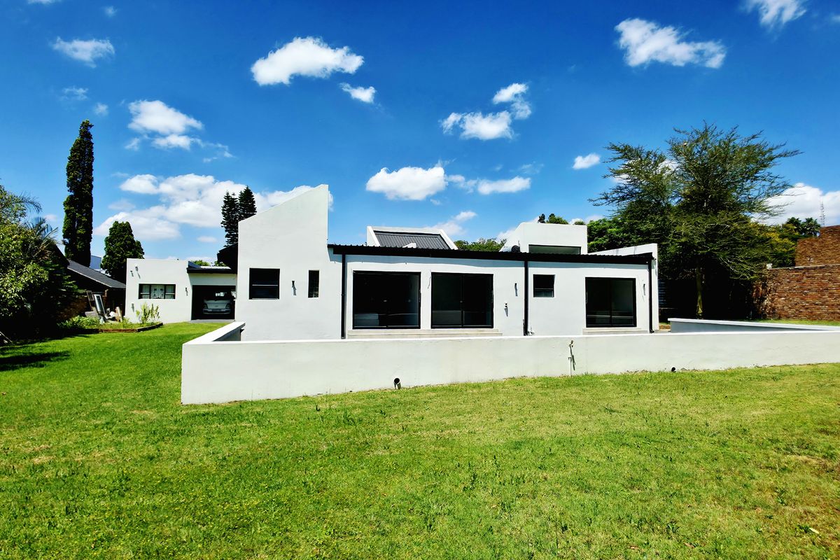 Rear view of a modern white house featuring large sliding glass doors, a low perimeter wall, and a spacious green lawn.