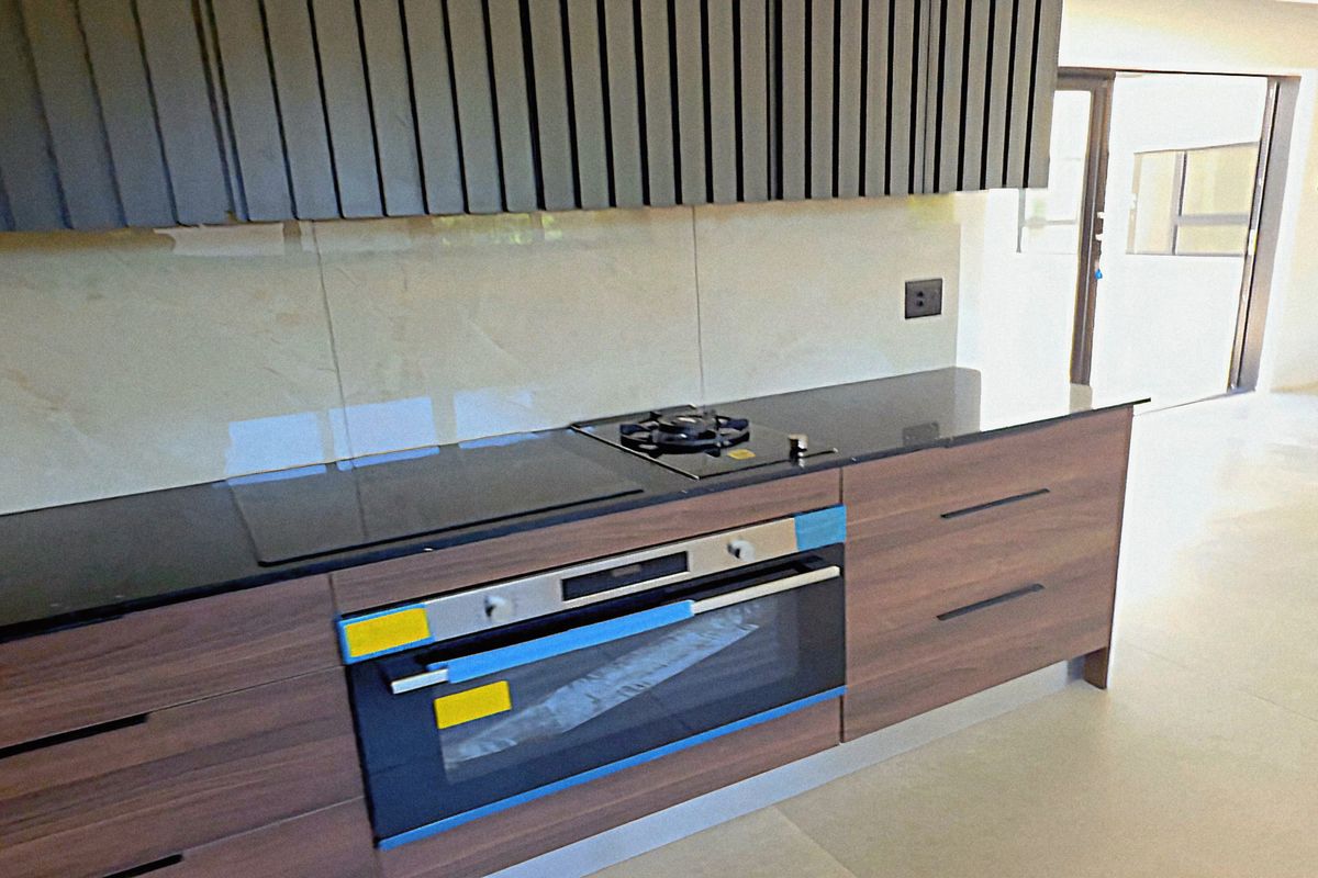 Modern kitchen featuring sleek wood-finish cabinetry, stone countertops, integrated gas and induction hobs, and a built-in oven with a contemporary glass splashback.