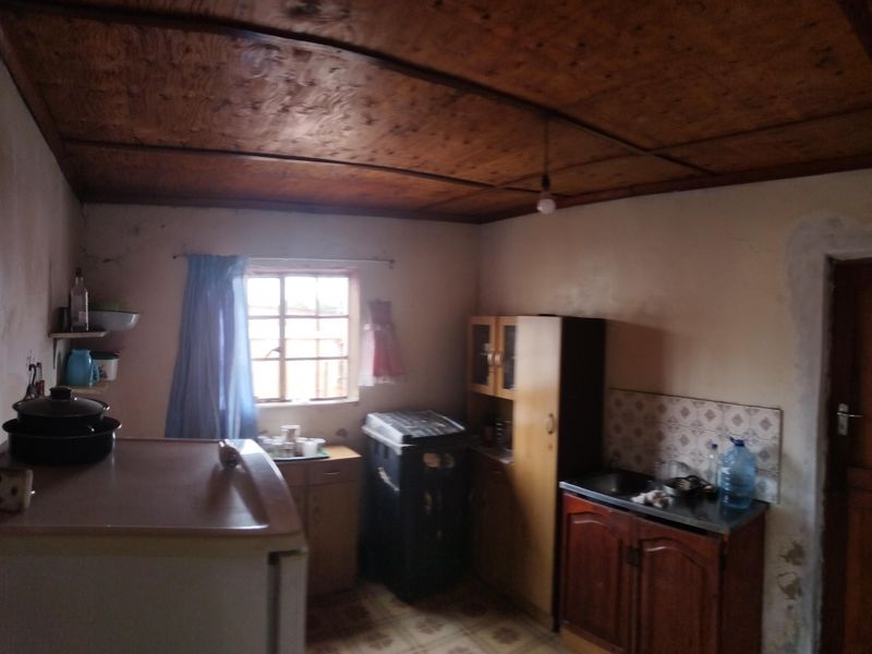 A dated kitchen featuring a wooden ceiling, basic cabinetry, and a tiled splashback, requiring significant renovation and cosmetic updates.